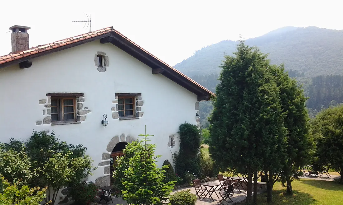El caserío de Natxiondo, encalado y con tejado rojo, visto desde el jardín con el monte detrás.