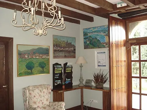 Rincón de estar con butaca de flores, cuadros de paisaje y una lámpara de araña.