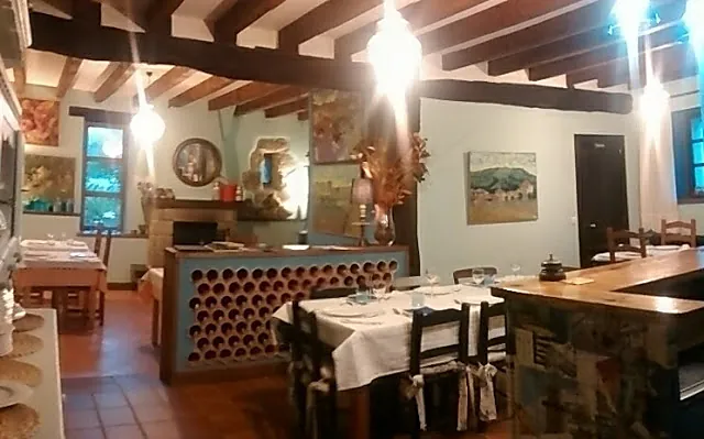 La taberna: barra de madera con botellero, mesas puestas con mantel blanco y vigas en el techo.