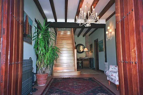 El zaguán con las puertas de madera oscura, la escalera al fondo y una alfombra en el suelo.